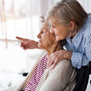 An elderly mother with her daughter at home looking out of the window. A carer assisting a disabled senior woman in wheelchair.